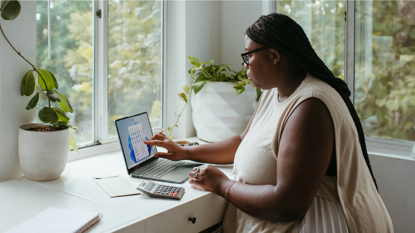 Businesswoman calculating finances on a laptop in a bright home office, exemplifying the benefits of remote work for businesses.
