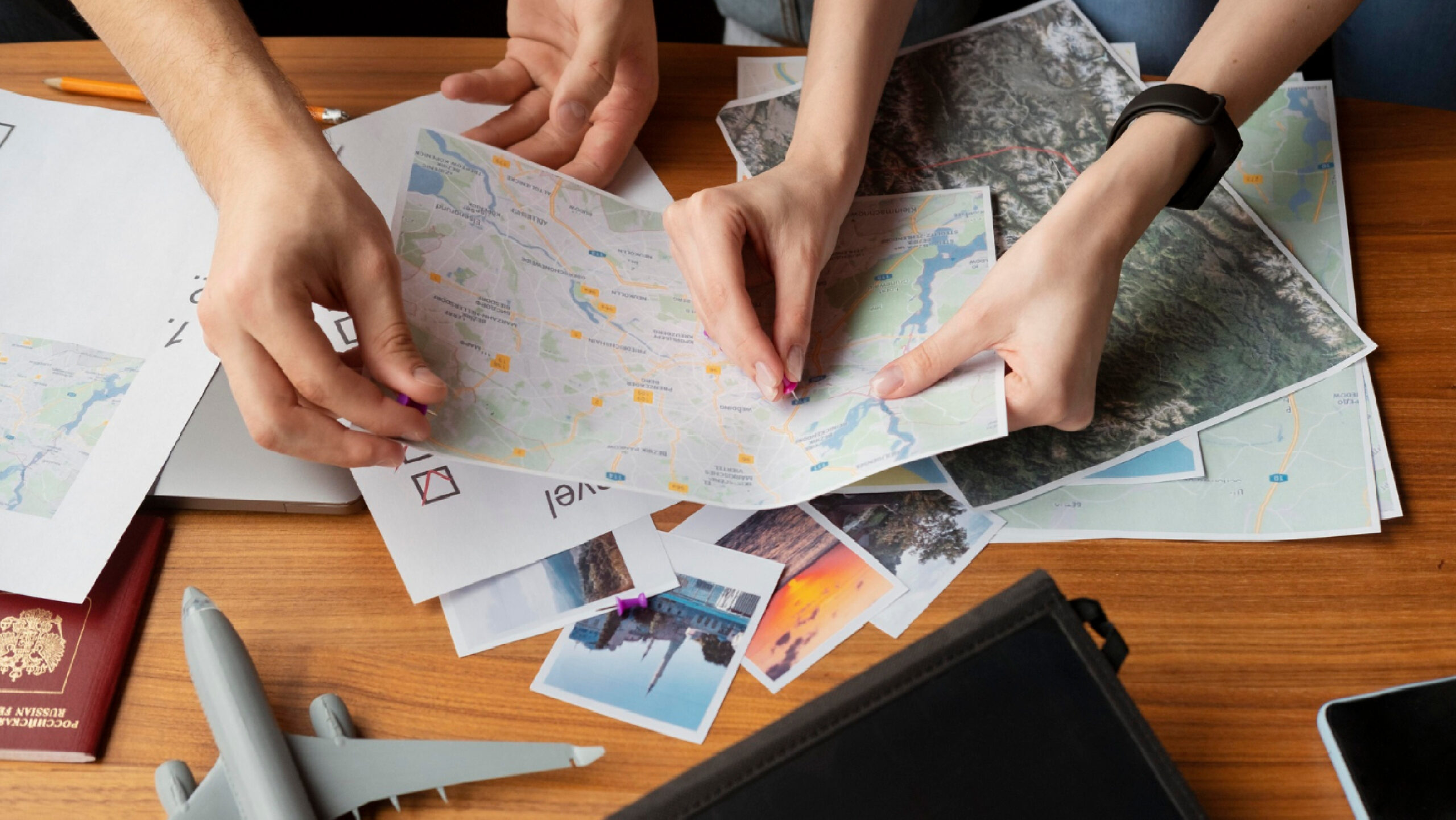 Hands planning a trip with maps and travel photos, highlighting the digital nomad lifestyle.
